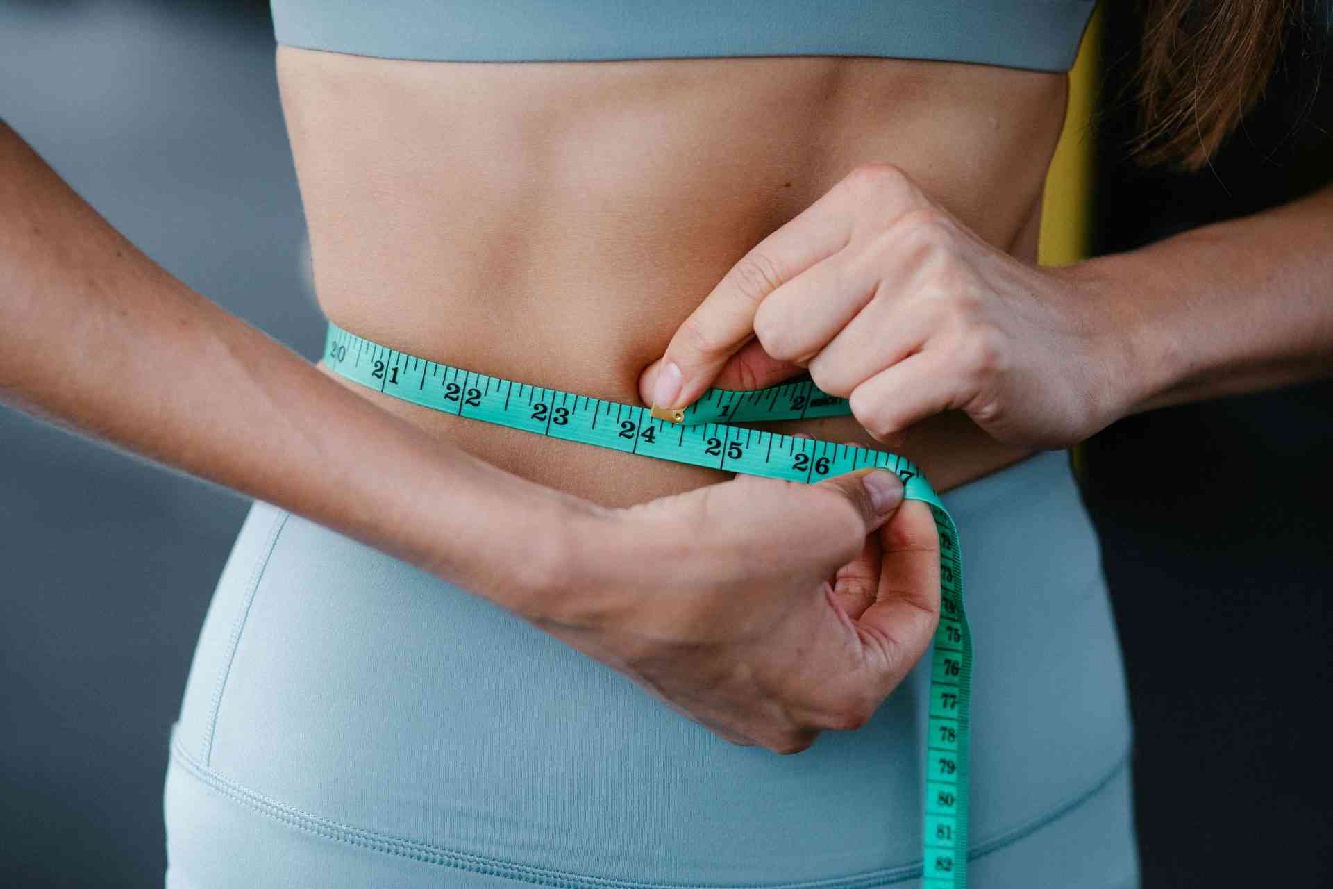 Primer plano de una mujer midiéndose la cintura con una cinta métrica, representando el fitness, la salud y la pérdida de peso.